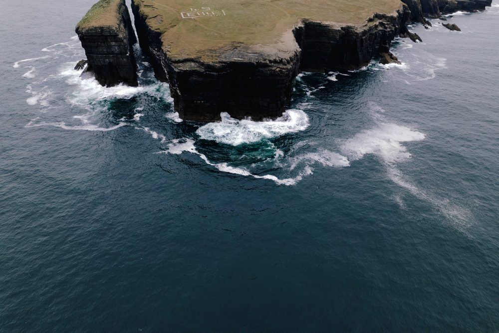 Green cliffs above a grey sea, seen from the air